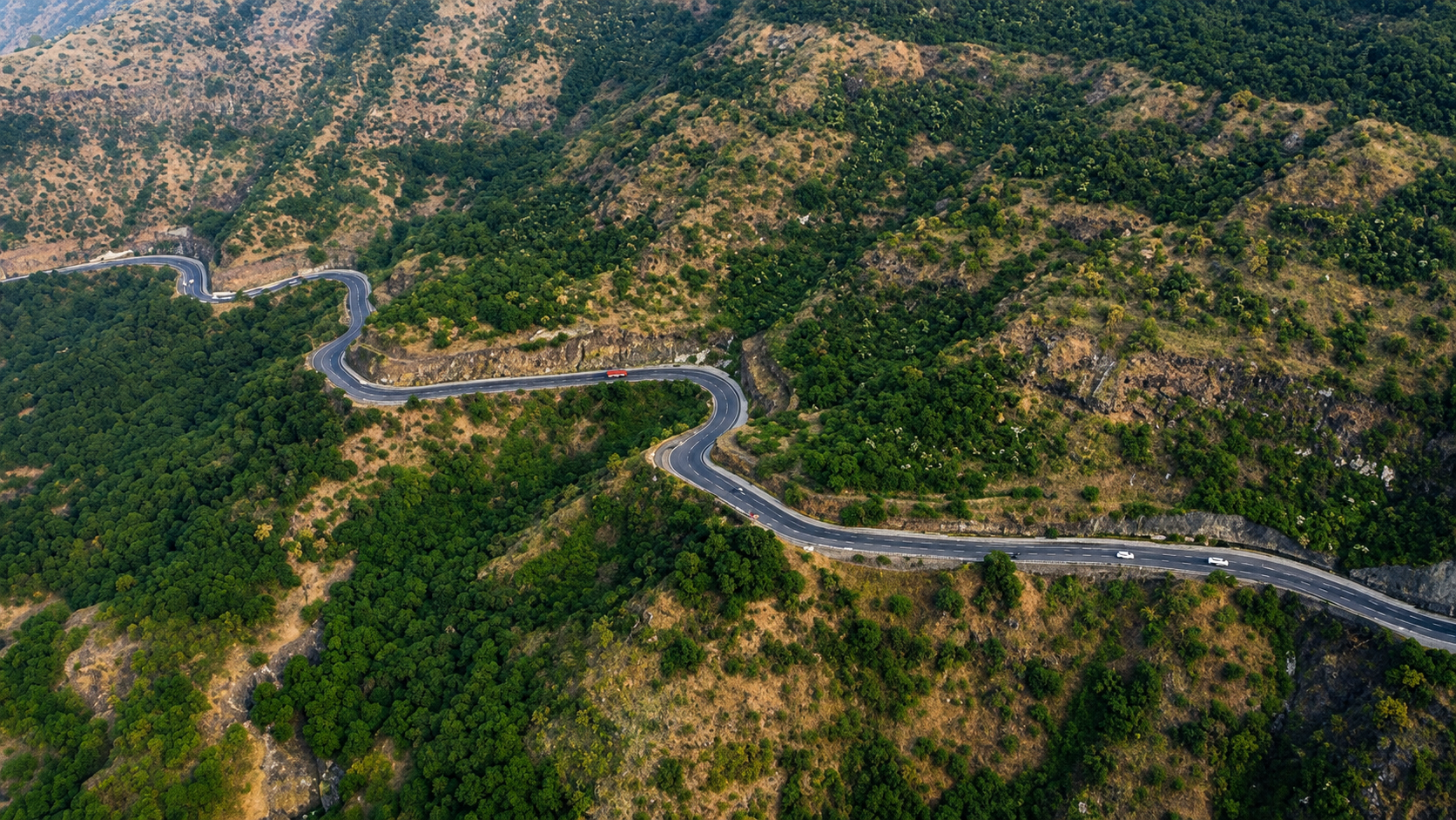 Aerial view of a winding two-lane highway snaking through forested hills