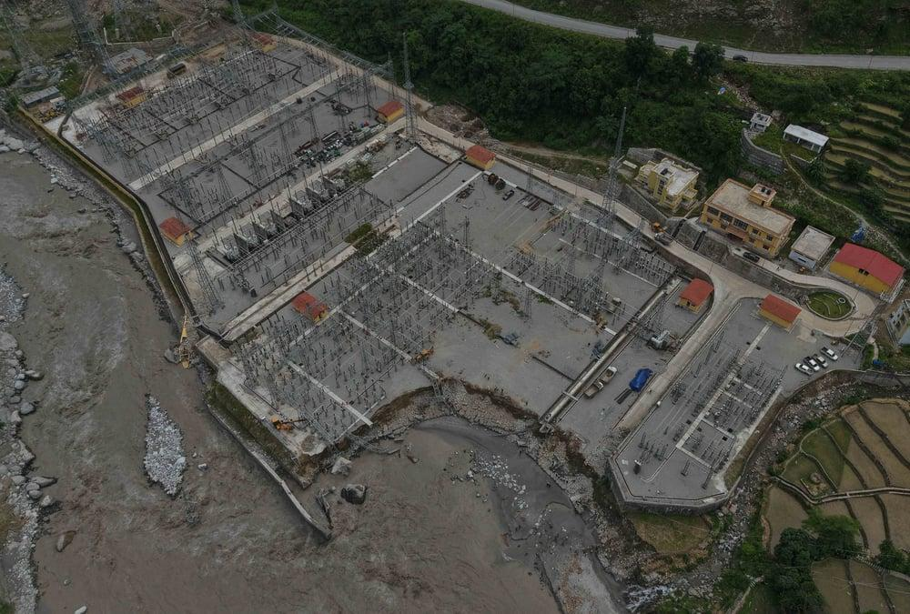 Aerial view of an electrical substation on a hillside beside a flood-scoured river channel